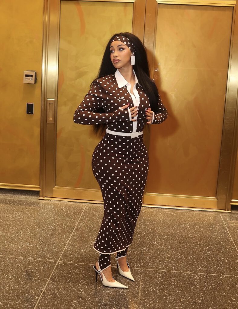 Cardi B is wearing a brown and white polka dot midi skirt set with a matching headband and white heels — celebrity street style fashion 2026