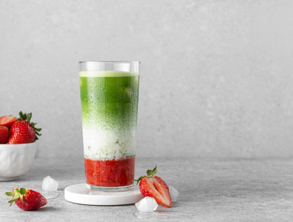 Strawberry matcha for spring latte served in high ball glass with ice cubes, fresh berries, strawberry puree and matcha green tea.